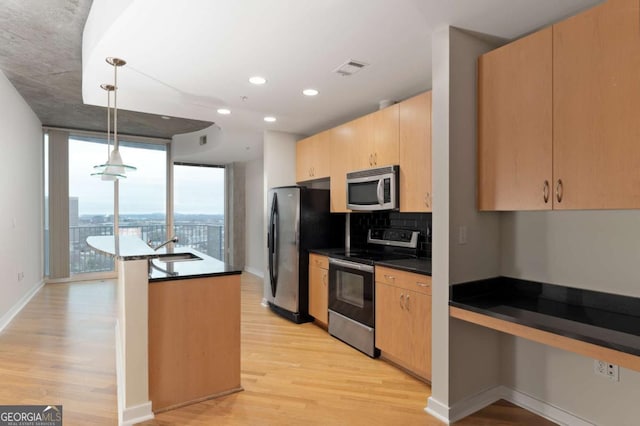 kitchen with appliances with stainless steel finishes, light brown cabinetry, light hardwood / wood-style floors, and pendant lighting