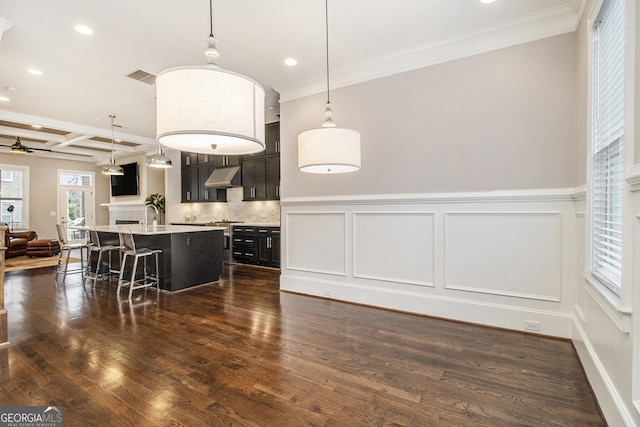 kitchen with crown molding, a breakfast bar, coffered ceiling, a center island with sink, and decorative light fixtures