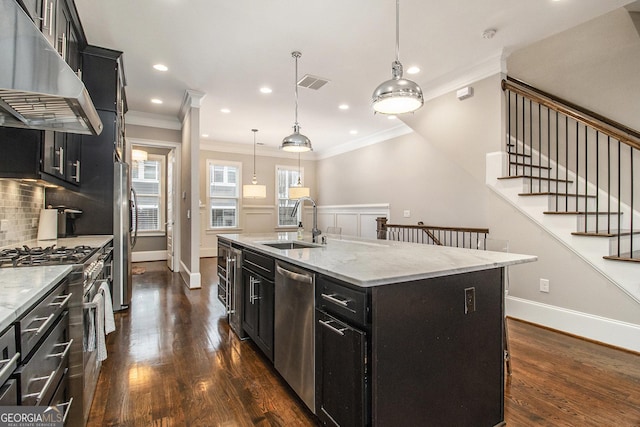 kitchen with sink, hanging light fixtures, stainless steel appliances, light stone countertops, and a center island with sink