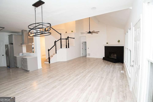 unfurnished living room featuring ceiling fan with notable chandelier, light wood-type flooring, and vaulted ceiling