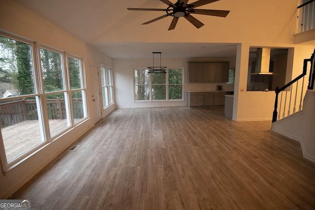 unfurnished living room with vaulted ceiling, plenty of natural light, wood-type flooring, and ceiling fan with notable chandelier