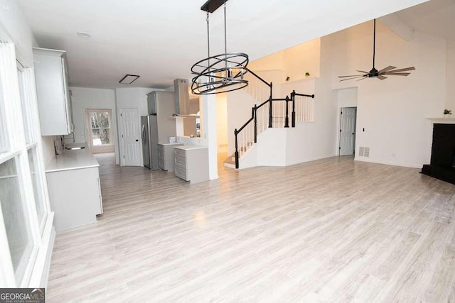 unfurnished living room with sink, ceiling fan with notable chandelier, and light wood-type flooring