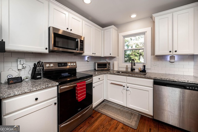 kitchen featuring white cabinets, stainless steel appliances, dark hardwood / wood-style flooring, light stone counters, and sink