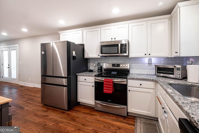 kitchen featuring light stone counters, dark wood-type flooring, stainless steel appliances, backsplash, and white cabinetry