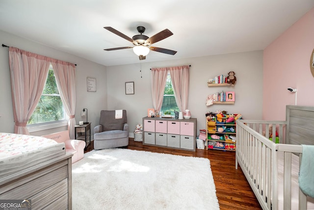 bedroom with dark hardwood / wood-style flooring, a nursery area, ceiling fan, and multiple windows