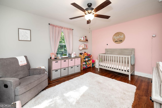 bedroom with ceiling fan, dark hardwood / wood-style floors, and a nursery area