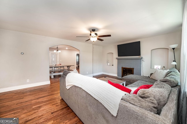 living room featuring ceiling fan with notable chandelier, a fireplace, and hardwood / wood-style floors