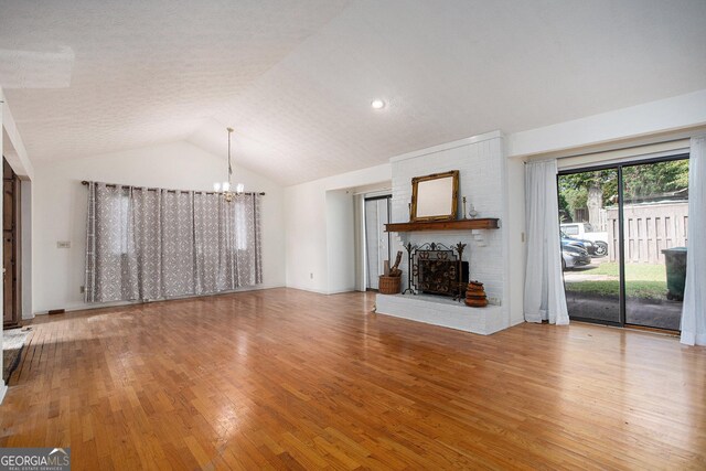 unfurnished living room with hardwood / wood-style flooring, lofted ceiling, a brick fireplace, and a notable chandelier