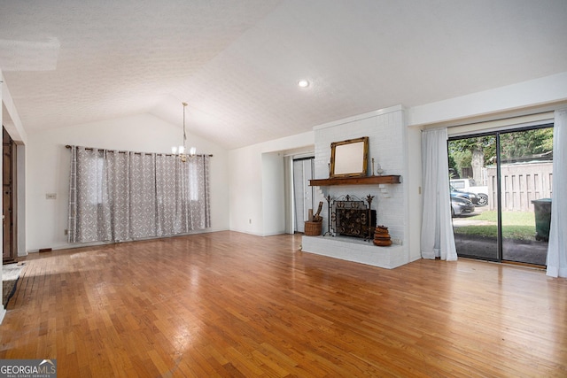 unfurnished living room with a brick fireplace, hardwood / wood-style flooring, vaulted ceiling, and a chandelier