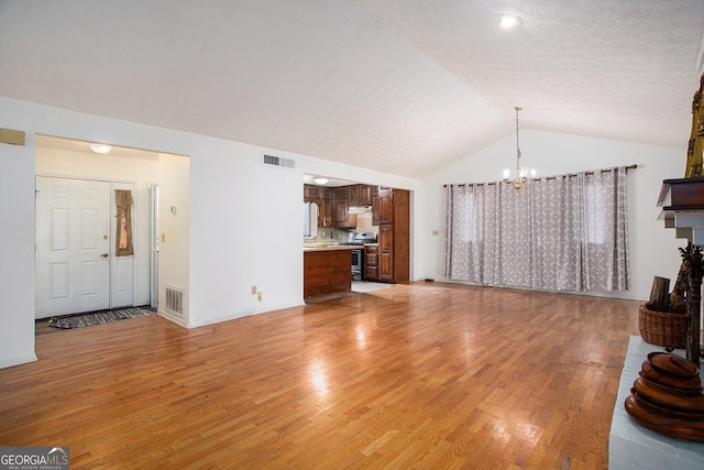 unfurnished living room featuring an inviting chandelier, light hardwood / wood-style flooring, and lofted ceiling