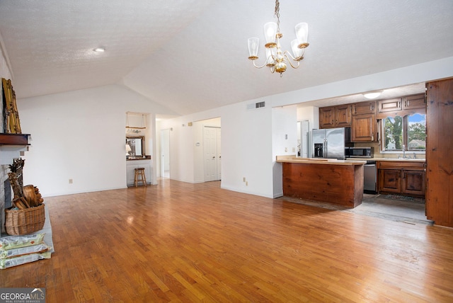 unfurnished living room featuring an inviting chandelier, lofted ceiling, sink, a textured ceiling, and light hardwood / wood-style flooring