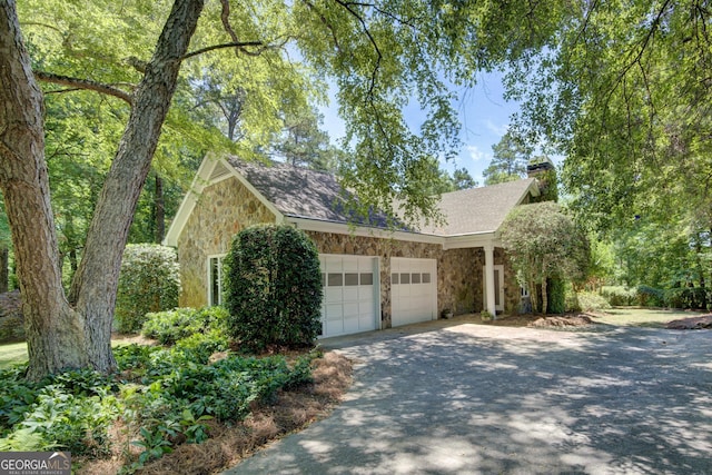 view of front of home featuring roof with shingles, a chimney, an attached garage, stone siding, and driveway