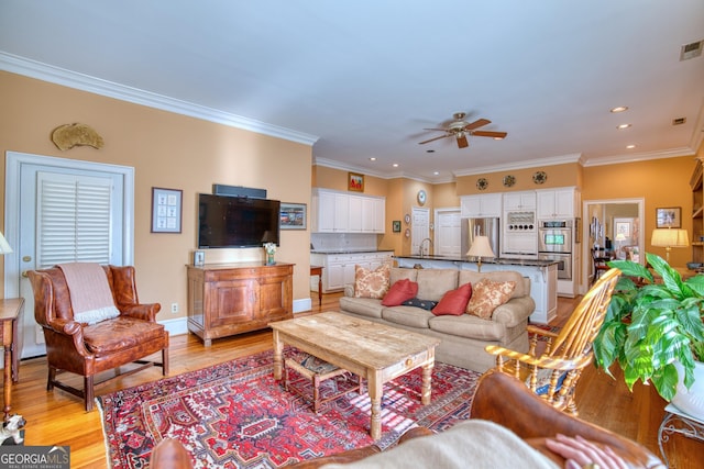 living room with visible vents, ornamental molding, light wood-style flooring, and a ceiling fan