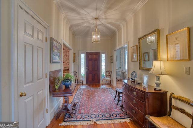 entryway with crown molding, an inviting chandelier, and wood finished floors