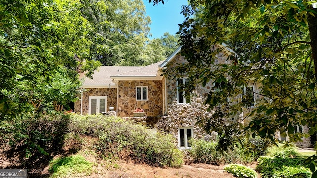 view of front of home with a shingled roof, stone siding, and french doors