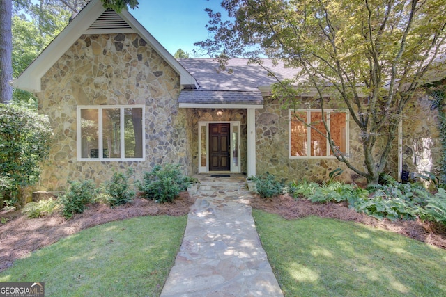 view of front of home with stone siding, a shingled roof, and a front yard