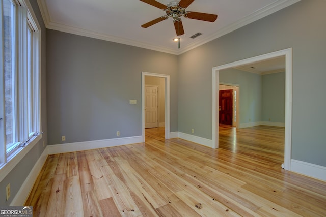 empty room featuring light wood-style flooring, visible vents, baseboards, and ornamental molding