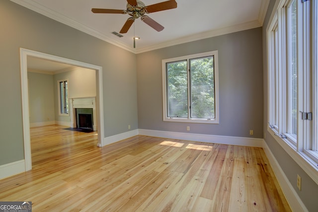 spare room featuring a fireplace with flush hearth, baseboards, light wood-style flooring, and crown molding