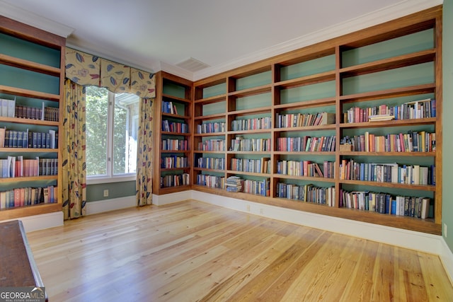 unfurnished room with wall of books, visible vents, wood finished floors, and ornamental molding