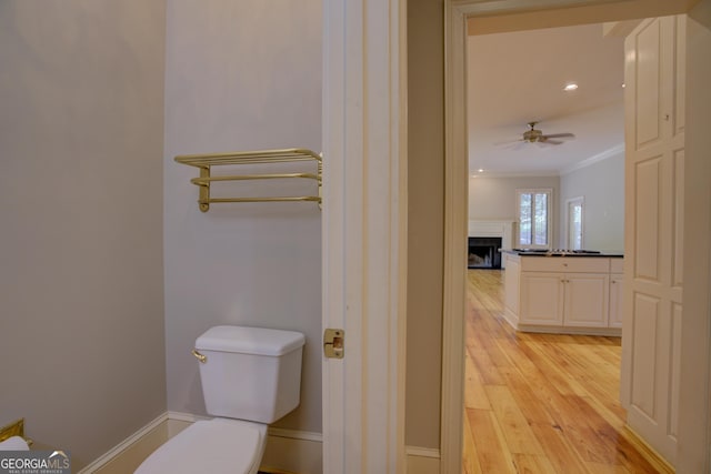 half bathroom with toilet, a fireplace, wood finished floors, a ceiling fan, and ornamental molding