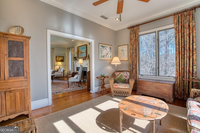 sitting room with baseboards, wood finished floors, visible vents, and crown molding