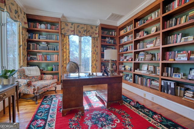 office with wall of books, wood finished floors, visible vents, and crown molding