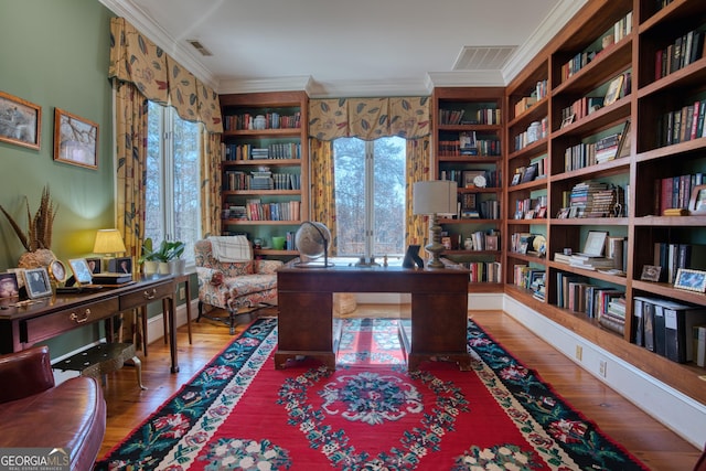 office with wall of books, visible vents, crown molding, and wood finished floors