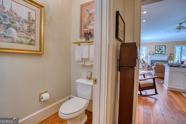 bathroom featuring baseboards, a ceiling fan, toilet, hardwood / wood-style flooring, and a fireplace