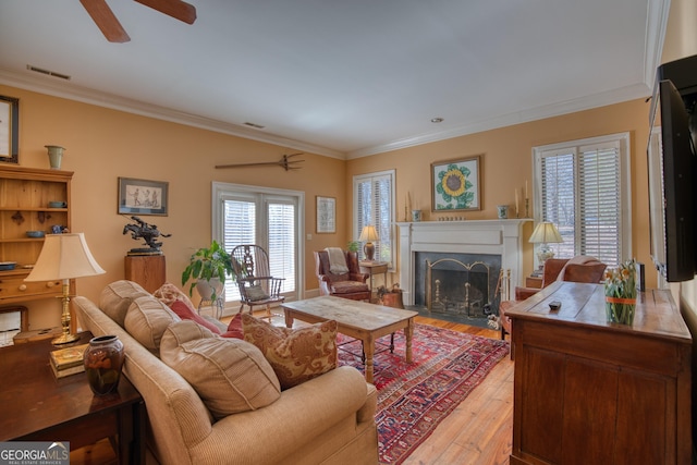 living room featuring visible vents, a fireplace with flush hearth, ceiling fan, ornamental molding, and light wood-type flooring