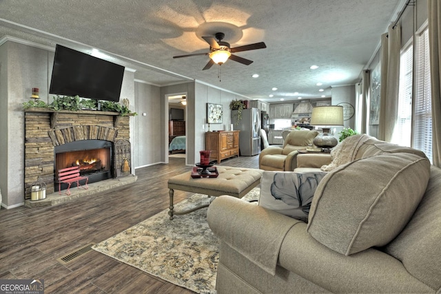 living room with ornamental molding, a textured ceiling, ceiling fan, a fireplace, and dark hardwood / wood-style floors