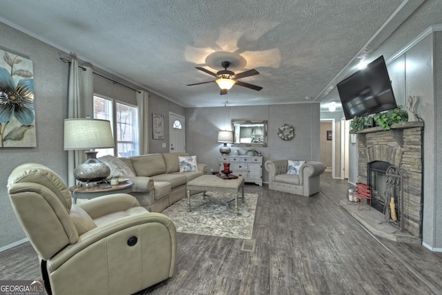 living room featuring dark wood-type flooring, a stone fireplace, ceiling fan, ornamental molding, and a textured ceiling