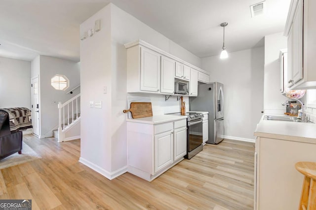 kitchen featuring white cabinets, sink, light wood-type flooring, appliances with stainless steel finishes, and decorative light fixtures