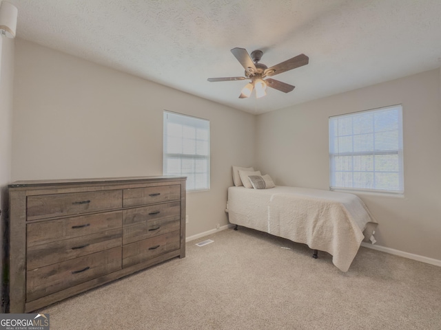 carpeted bedroom featuring ceiling fan, a textured ceiling, and multiple windows