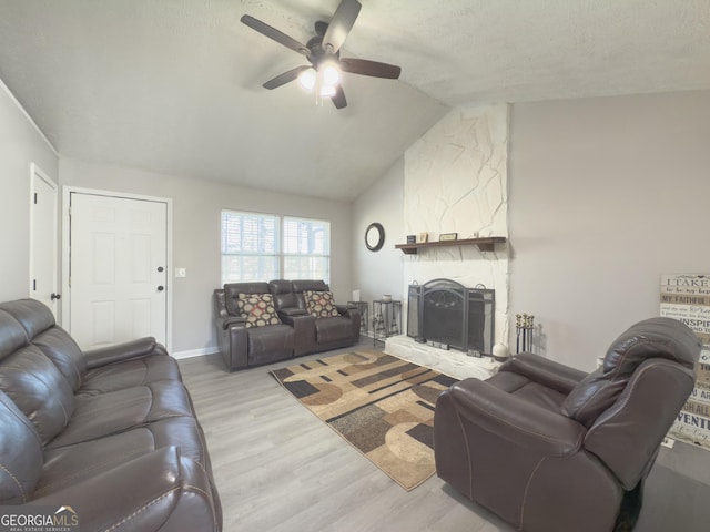 living room with ceiling fan, a stone fireplace, light hardwood / wood-style floors, a textured ceiling, and vaulted ceiling