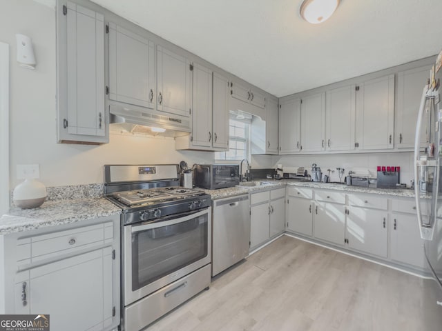 kitchen featuring appliances with stainless steel finishes, light hardwood / wood-style floors, light stone counters, and sink