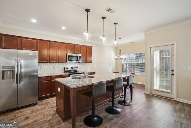 kitchen featuring light stone countertops, appliances with stainless steel finishes, sink, decorative light fixtures, and an island with sink