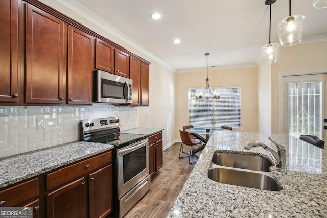 kitchen featuring light stone counters, sink, stainless steel appliances, and decorative light fixtures