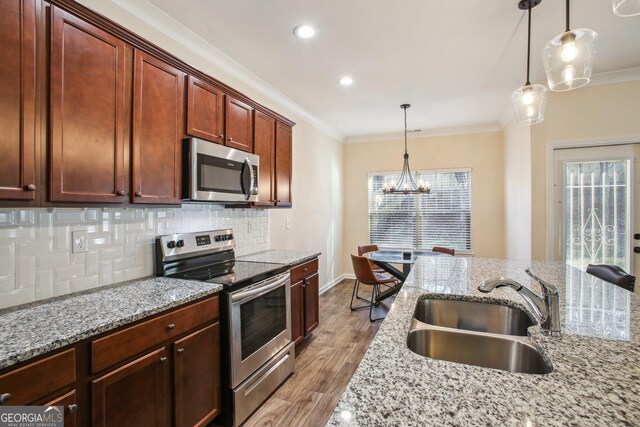 kitchen with sink, stainless steel appliances, hanging light fixtures, and light stone countertops