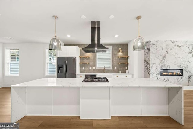 kitchen with wall chimney exhaust hood, tasteful backsplash, pendant lighting, stainless steel appliances, and light stone countertops