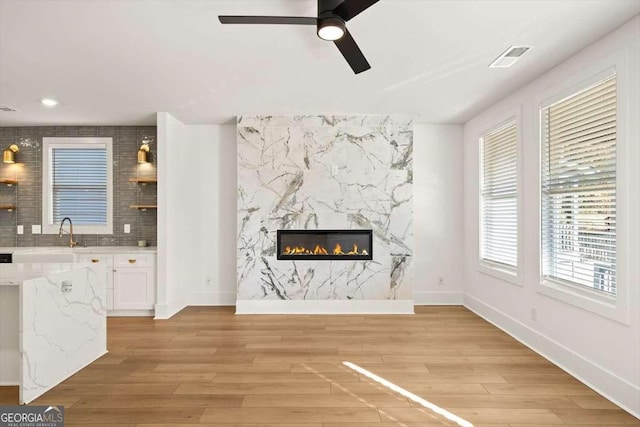 unfurnished living room with ceiling fan, a premium fireplace, light hardwood / wood-style flooring, and a wealth of natural light