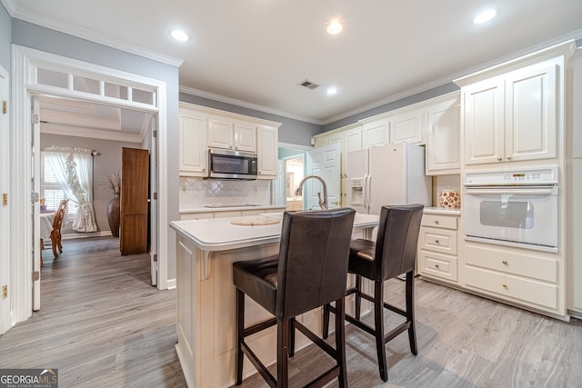 kitchen with white appliances, decorative backsplash, a breakfast bar, a center island with sink, and ornamental molding