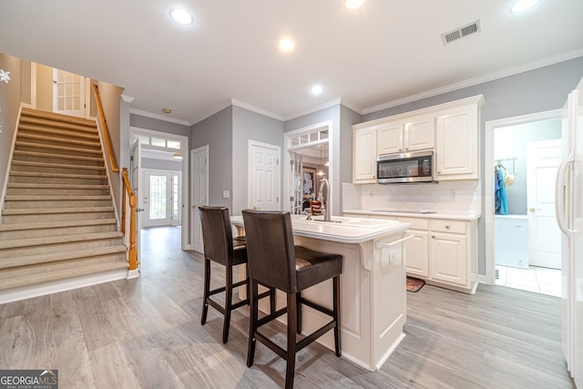 kitchen with light wood-type flooring, tasteful backsplash, ornamental molding, a center island with sink, and a breakfast bar area