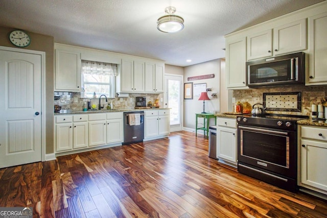 kitchen featuring appliances with stainless steel finishes, sink, dark stone countertops, white cabinets, and dark wood-type flooring