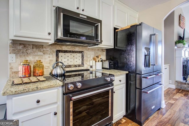 kitchen with appliances with stainless steel finishes, white cabinetry, tasteful backsplash, light stone countertops, and light hardwood / wood-style floors