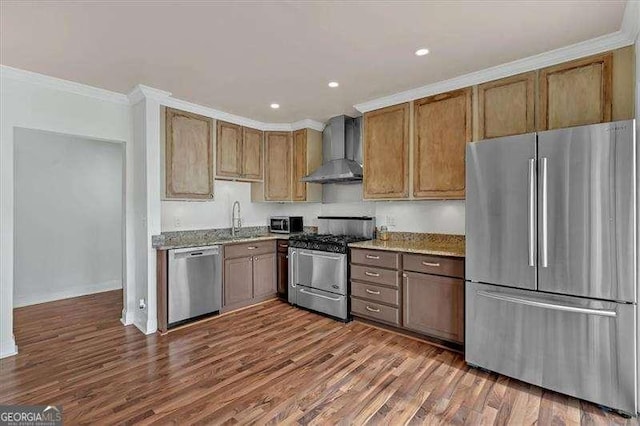 kitchen with light stone countertops, sink, stainless steel appliances, wall chimney range hood, and ornamental molding