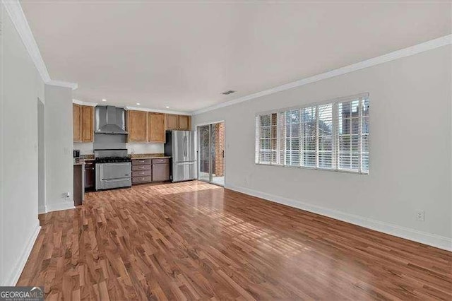 kitchen with dark hardwood / wood-style floors, ornamental molding, wall chimney range hood, and appliances with stainless steel finishes