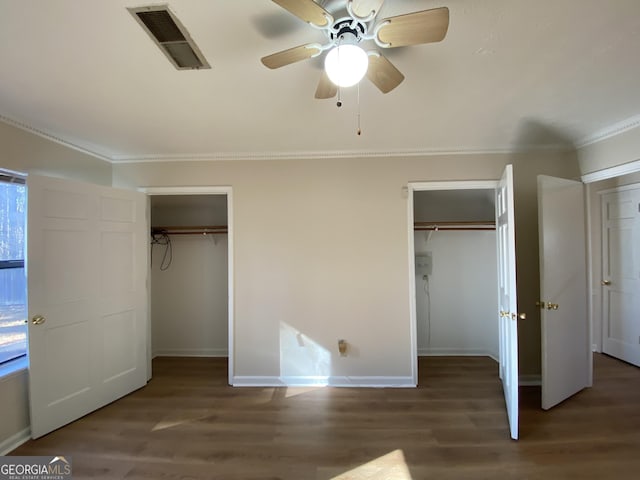 unfurnished bedroom with ceiling fan, crown molding, dark wood-type flooring, and two closets