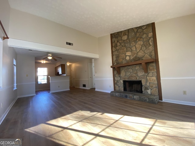 unfurnished living room with a stone fireplace, ceiling fan, dark hardwood / wood-style flooring, and a textured ceiling