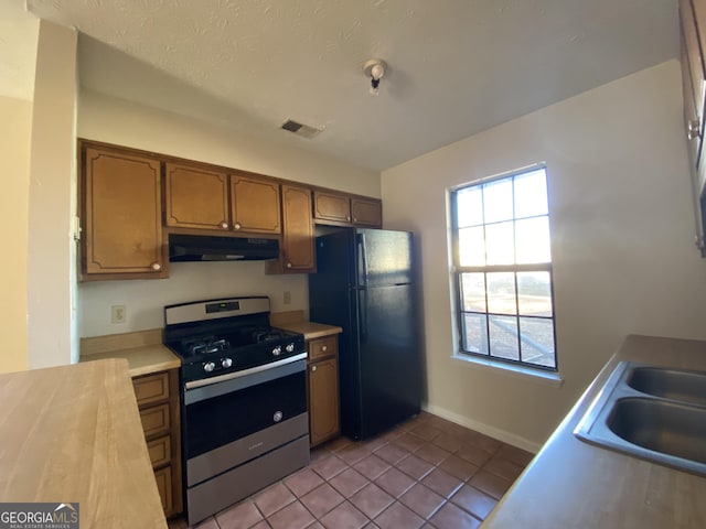 kitchen with stainless steel range, sink, a textured ceiling, black refrigerator, and light tile patterned flooring