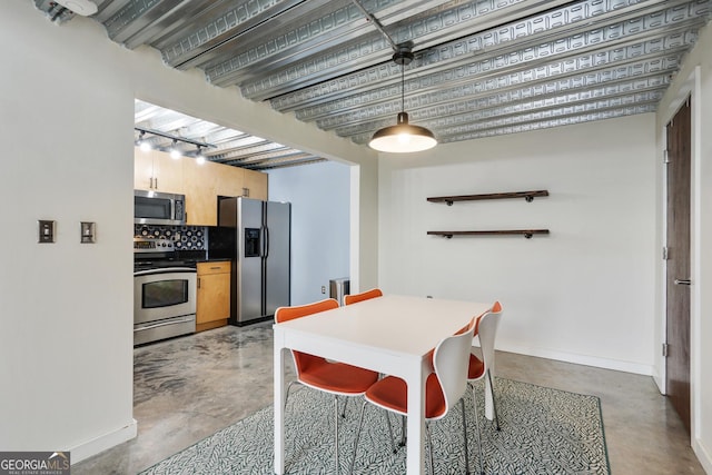 kitchen featuring concrete flooring, stainless steel appliances, hanging light fixtures, decorative backsplash, and dark countertops